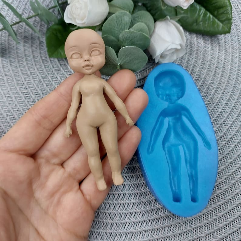 Puede incluir: Una figurita de mu&ntilde;eca de color carne con una cara detallada y un molde de silicona azul de una figurita de mu&ntilde;eca.