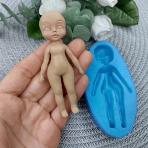 Puede incluir: Un molde de silicona para hacer una peque&ntilde;a figura de mu&ntilde;eca. El molde es azul y tiene una impresi&oacute;n detallada de una mu&ntilde;eca con cabeza, brazos, piernas y torso. Una mu&ntilde;eca terminada hecha con el molde se muestra junto al molde.