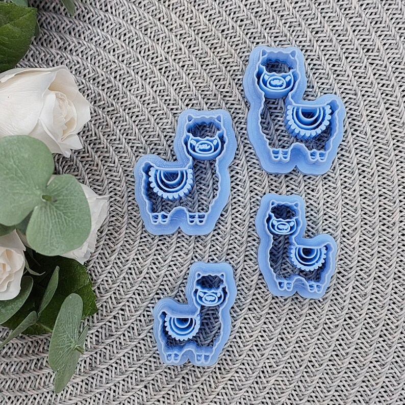 May include: Four blue plastic cookie cutters shaped like llamas. Each llama has a decorative design on its neck.