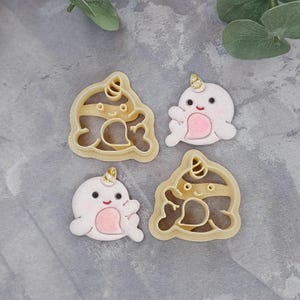 May include: Three cookie cutters shaped like narwhals. Two are beige and one is white. The beige cutters have a striped pattern and the white cutter has a pink heart.