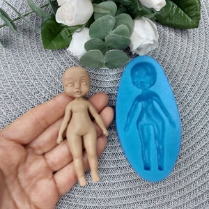 Puede incluir: Un molde de silicona para hacer una peque&ntilde;a figura de mu&ntilde;eca. El molde es azul y tiene un contorno detallado de una mu&ntilde;eca con brazos, piernas y cabeza. Una peque&ntilde;a mu&ntilde;eca hecha con el molde se muestra al lado.