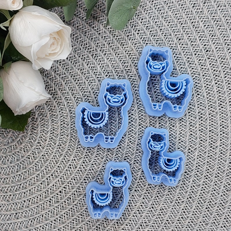 May include: Four blue plastic llama cookie cutters of varying sizes. The cutters are on a light blue textured surface.