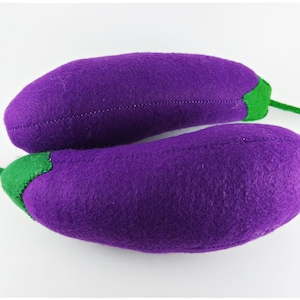 Puede incluir: Dos berenjenas de peluche en un vibrante tono púrpura, con tallos y tapas verdes. La textura suave, similar al fieltro, y los detalles cosidos dan a estas verduras hechas a mano un encanto caprichoso. Perfecto para la decoración de la cocina o el juego de los niños.