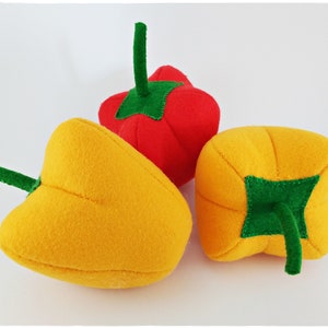 Puede incluir: Tres pimientos de fieltro, uno rojo, dos amarillos, con tallos de fieltro verde.
