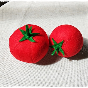 Può includere: Due pomodori di feltro rosso con foglie di feltro verde. I pomodori sono su una superficie bianca testurizzata.