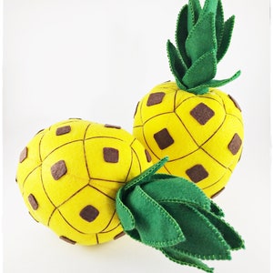 May include: Two felt pineapples with brown accents and green tops. The pineapples are yellow and have a textured surface.