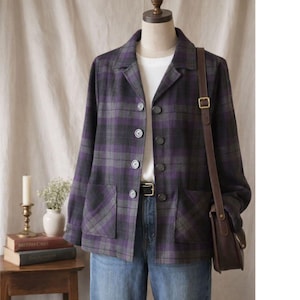 May include: A purple and grey checked blazer with a traditional collar and button fastening. The jacket features two front pockets and is worn with blue jeans. A brown leather shoulder bag is also visible.