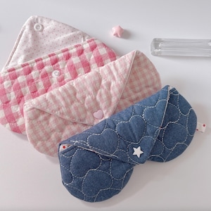 Könnte beinhalten: Drei gesteppte Augenmasken in Rosa und Blau. Eine Maske ist jeansblau mit Herzstichen und einem weißen Stern. Die anderen beiden sind rosa mit weißen Punkten und Vichy-Mustern. Jede Maske hat einen Knopfverschluss.