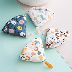 Puede incluir: Cuatro juguetes triangulares para bebés con tela estampada. Uno es azul marino con formas florales y geométricas, otro tiene diseños de cactus y setas, un tercero tiene osos y huesos, y el último tiene arcoíris y formas. Cada uno tiene un lazo de tela.