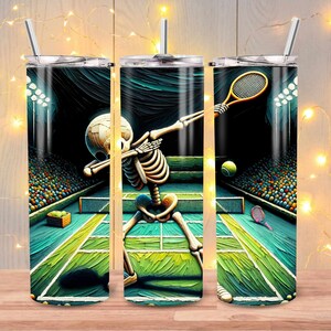 May include: A stainless steel tumbler with a colorful illustration of a skeleton doing a dab dance on a tennis court. The skeleton is holding a tennis racket and there are tennis balls on the court. The background is a tennis stadium with spectators.