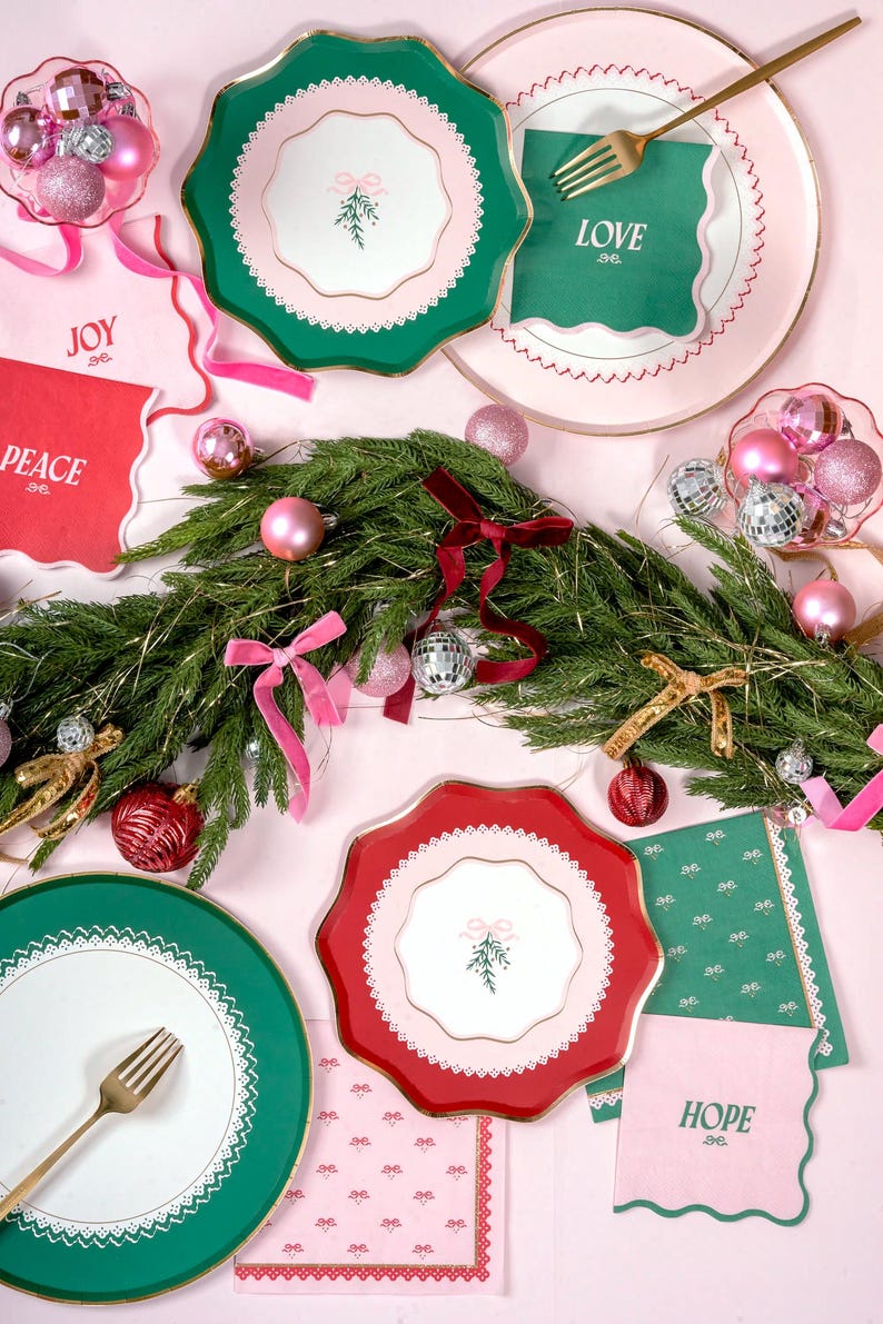 Puede incluir: Una mesa de Navidad festiva con platos de papel verde y rojo, servilletas y tenedores dorados. Las servilletas muestran las palabras "Love", "Hope", "Joy" y "Peace".