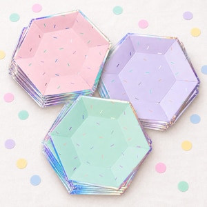 May include: Three stacks of hexagonal paper plates in pastel pink, lavender, and mint green. Each plate features a metallic iridescent rim and a scattered pattern of small, thin, multi-colored confetti-like dashes across the flat surface.