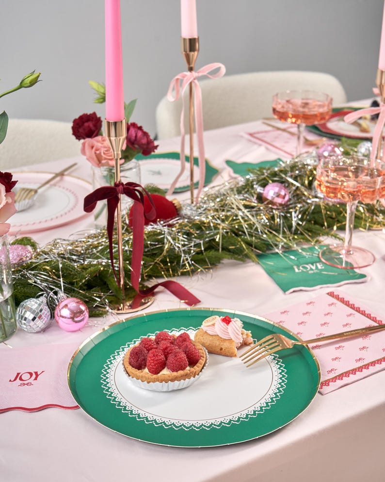 Puede incluir: Un plato de papel verde y blanco con un borde de encaje. El plato tiene un borde dorado y est&aacute; decorado con una tarta de frambuesas y una crema de hojaldre. El plato est&aacute; sobre un mantel rosa con una servilleta rosa y blanca que dice "JOY".