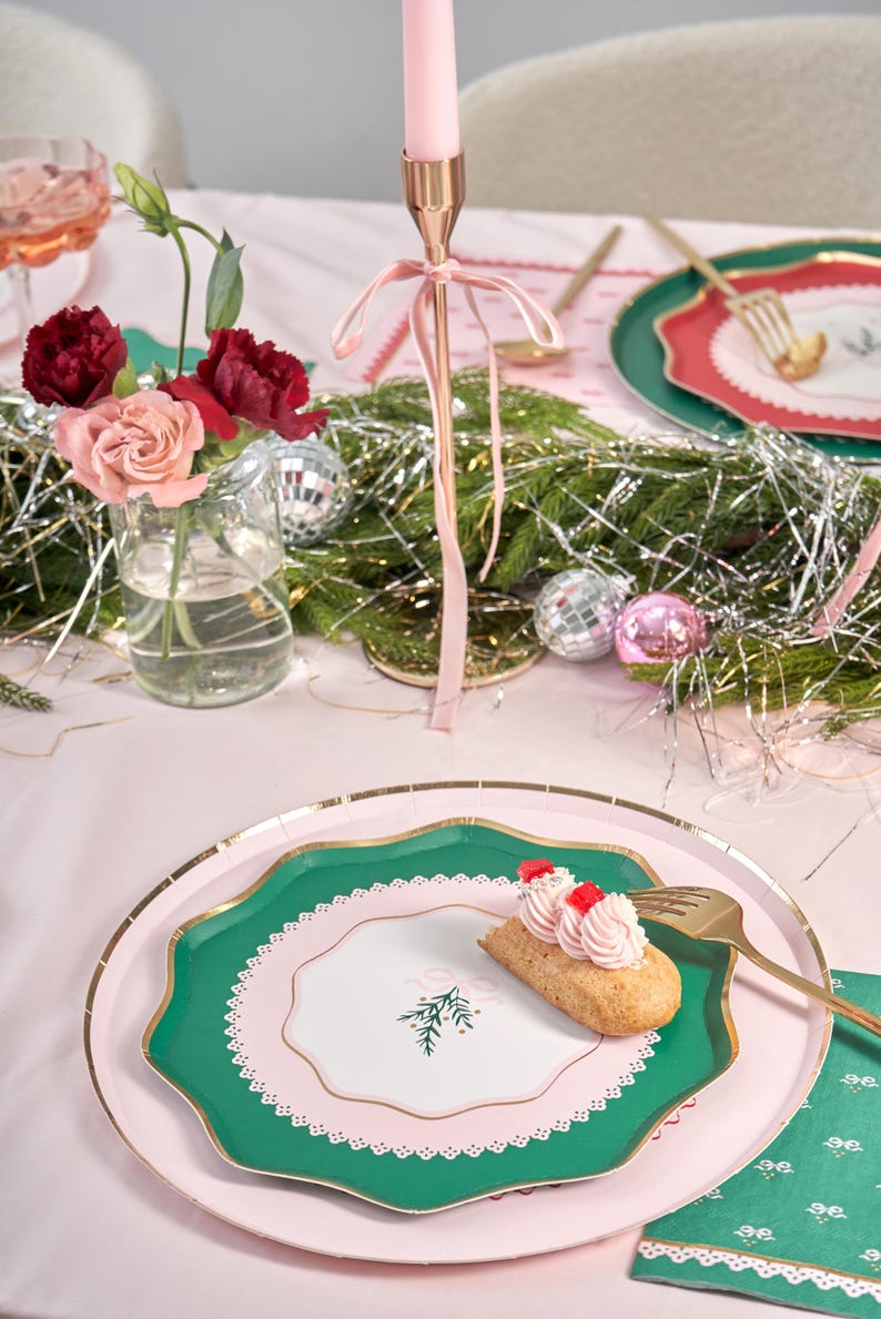 Puede incluir: Un plato de papel verde y rosa con un borde dorado y un centro blanco con un dise&ntilde;o de rama de pino verde. Un peque&ntilde;o pastel con glaseado rosa y chispas rojas est&aacute; en el plato.
