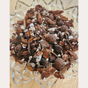 May include: A close-up of a mixture of brown bark chips, white perlite, and small brown balls. The mixture is in a clear glass bowl with a starburst pattern.