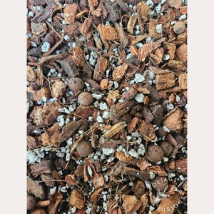 May include: Close-up of a mixture of brown and white potting soil. The soil is made up of small pieces of bark, coconut husk, and white perlite.