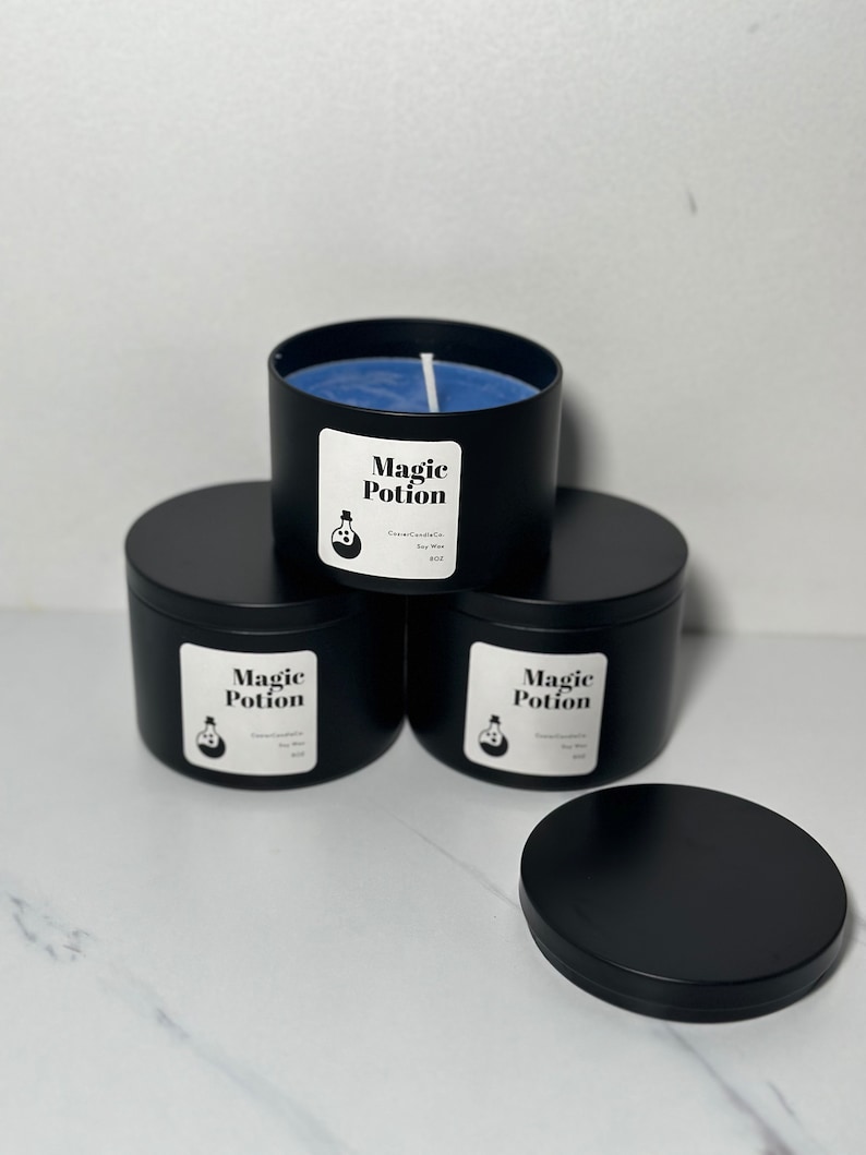 以下が含まれることがあります： 青いワックスと蓋が付いた黒いキャンドルジャーが4つ。ジャーには、「マジックポーション」という文字と、ポーションボトルの小さなイラストが描かれた白いラベルが付いています。