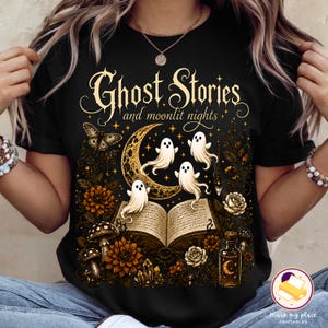 May include: A black t-shirt featuring a graphic print with the text "Ghost Stories and moonlit nights". The design includes three white ghosts, a crescent moon, an open book, mushrooms, flowers, a moth, crystals, and a small glass bottle.