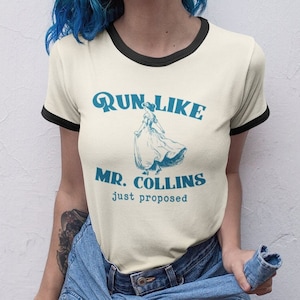 Puede incluir: Una camiseta blanca con cuello de canalé negro. La camiseta tiene un gráfico azul que dice "Run Like Mr. Collins just proposed" con una ilustración vintage de una mujer corriendo.