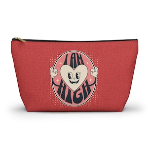 May include: Red zippered pouch with a retro-style graphic of a heart with eyes and arms, saying "I AM HIGH".