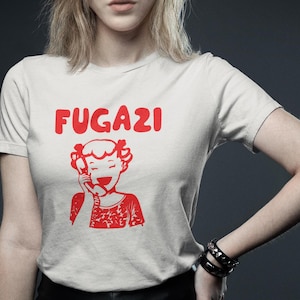 May include: White t-shirt with a red graphic of a cartoon girl on the phone and the word "FUGAZI" above her.