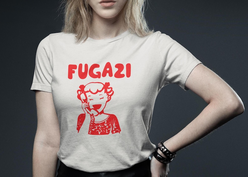 May include: White t-shirt with a red graphic of a cartoon girl on the phone and the word "FUGAZI" above her.