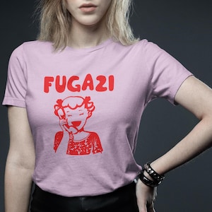 May include: Pink t-shirt with a red graphic of a girl on the phone and the word "FUGAZI" above her.