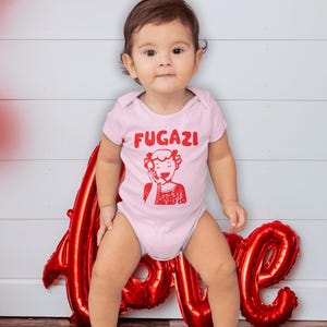 May include: A baby wearing a pink bodysuit with the word "FUGAZI" and a red cartoon image of a woman on the phone. The baby is sitting in front of a red foil balloon that says "LOVE".