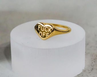 May include: A gold heart-shaped ring with the words "FUCK OFF" engraved on the front.