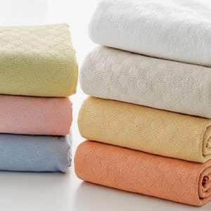 May include: A stack of six waffle weave blankets in various pastel colours, including light yellow, pink, blue, and peach.
