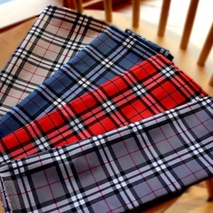 May include: Four plaid fabric squares in different colours, including grey, blue, red, and beige. The squares are stacked on top of each other, with the grey square on the bottom and the beige square on top.