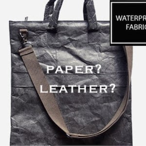 May include: A gray tote bag made of waterproof fabric with the text "PAPER? LEATHER?" printed on the front. The bag has a long adjustable strap and a zipper closure.
