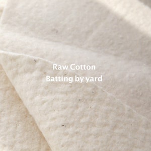 May include: Close-up of white raw cotton batting, showing the texture of the material. The text "Raw Cotton Batting by yard" is printed on the fabric.