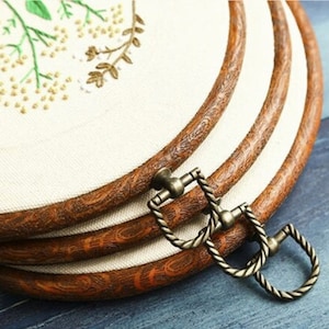 May include: Three wooden embroidery hoops with a floral embroidery design on the fabric. The hoops are stacked on top of each other and have a brass clasp.