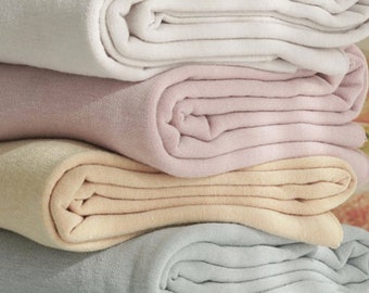 May include: Four folded blankets in different colors: white, pink, beige, and light blue. The blankets are stacked on top of each other.