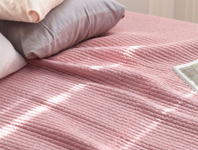 Puede incluir: Una colcha de cama suave y rosa acolchada con una textura acanalada sutil. La colcha est&aacute; hecha de una tela ligera y es perfecta para agregar un toque de color y comodidad a cualquier dormitorio.