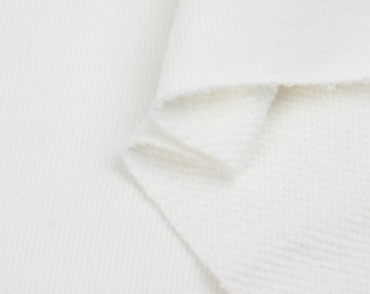 May include: Close-up of a white cotton fabric with a textured waffle weave. The fabric is folded over itself, showing the soft and comfortable texture.