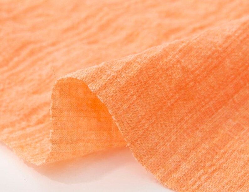 May include: Close-up of a soft, peach-colored fabric with a textured weave. The fabric is folded and draped, showing its texture and color.