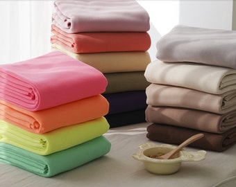 May include: A stack of colorful fleece blankets in various shades of pink, orange, yellow, green, beige, brown, and gray. The blankets are folded and stacked on top of each other.