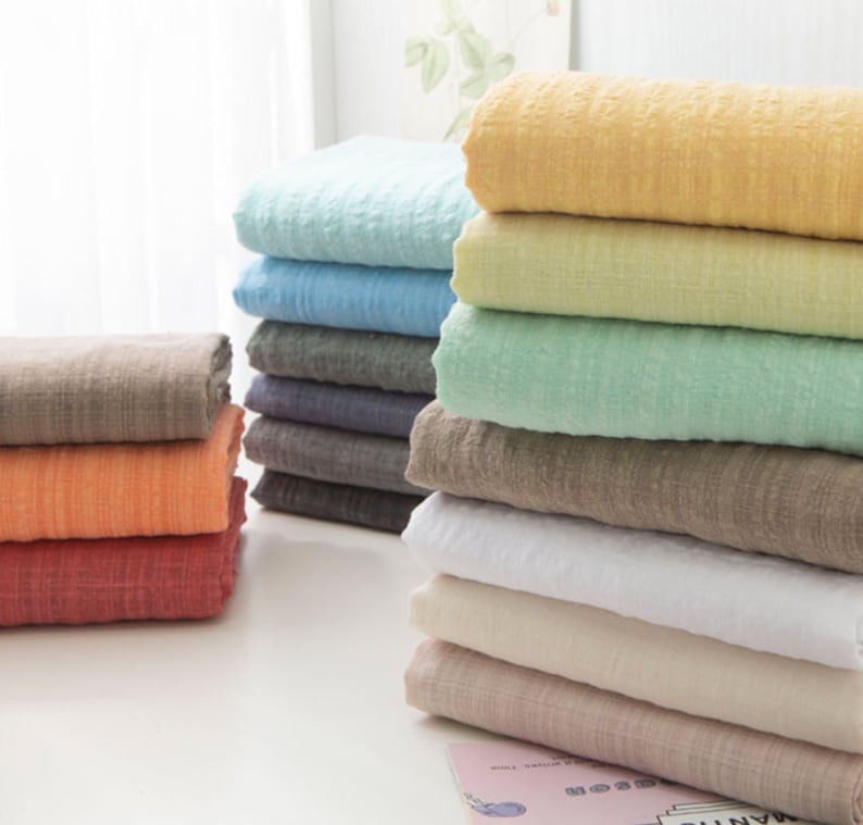 May include: A stack of 10 different colored fabric squares. The fabric is a soft, textured gauze. The colors are light blue, yellow, green, brown, white, beige, and pink.
