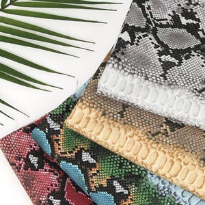May include: A stack of different patterned fabric swatches. The top swatch is a grey and black snake skin pattern, the second is a light beige with a textured pattern, the third is a brown and beige snake skin pattern, the fourth is a blue and green snake skin pattern, and the bottom swatch is a pink and red snake skin pattern.