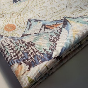 Peut inclure: Un tissu blanc avec un motif imprimé de montagnes, d'arbres et d'une carte. Le tissu est plié en trois.