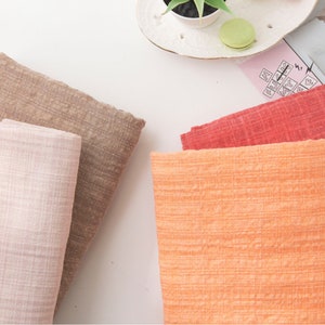 May include: Four fabric swatches in different colors and textures. The swatches are pink, brown, orange, and red. The swatches are arranged in a row on a white surface.