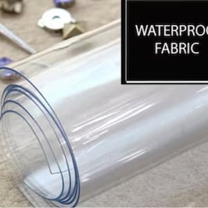 May include: A roll of clear, transparent, waterproof fabric. The fabric is rolled up tightly and is ready to be unrolled. The text "Waterproof Fabric" is printed on a black background.