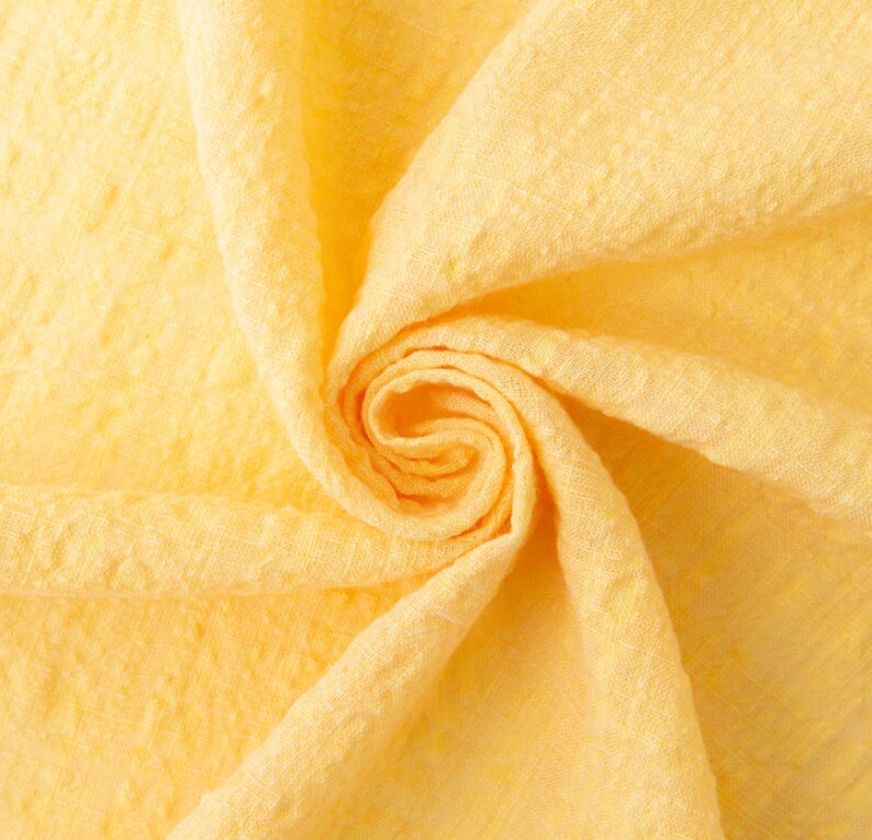 May include: A close-up of a yellow fabric with a textured surface. The fabric is folded and twisted into a spiral shape.