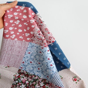 May include: A patchwork fabric featuring a variety of floral patterns in pink, blue and white. The fabric is made up of six different squares, each with a unique pattern.