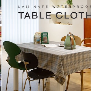 Peut inclure: Une table blanche avec une nappe à carreaux gris et noirs. La table est dressée avec une théière, une tasse, un livre et une boîte de craquelins. La table est entourée de quatre chaises, dont deux sont vertes et deux sont noires. Le texte "Laminate Waterproof Table Cloth" est affiché au-dessus de la table.