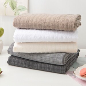 May include: A stack of four fabric swatches in different colors and textures. The swatches are folded and arranged in a pyramid shape. The top swatch is a light brown color, the second swatch is white, the third swatch is a light beige color, and the bottom swatch is a dark gray color.