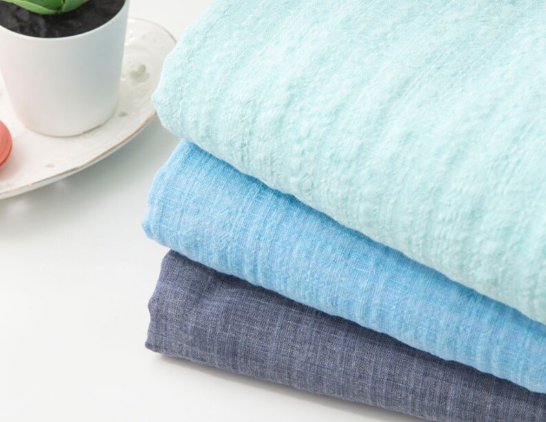 May include: Three pieces of fabric stacked on top of each other. The top piece is a light blue color, the middle piece is a medium blue color, and the bottom piece is a dark blue color.