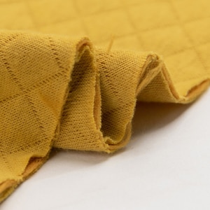 Puede incluir: Primer plano de una tela acolchada amarilla con una superficie texturizada. La tela está doblada y muestra el detalle de las costuras.